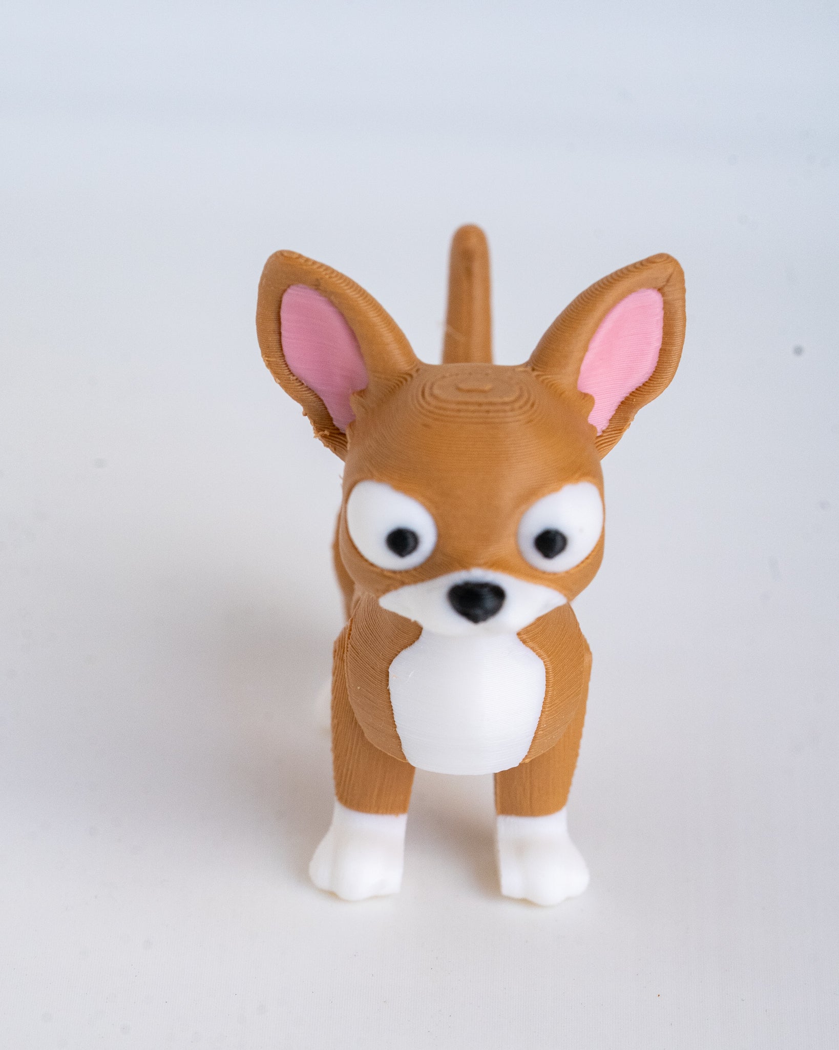 A small brown and white dog figurine with pink inner ears, photographed against a plain light gray background.