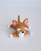 A small brown dog-shaped figurine or toy with pink inner ears, white paws and chest, black eyes and nose, photographed on a plain light background.