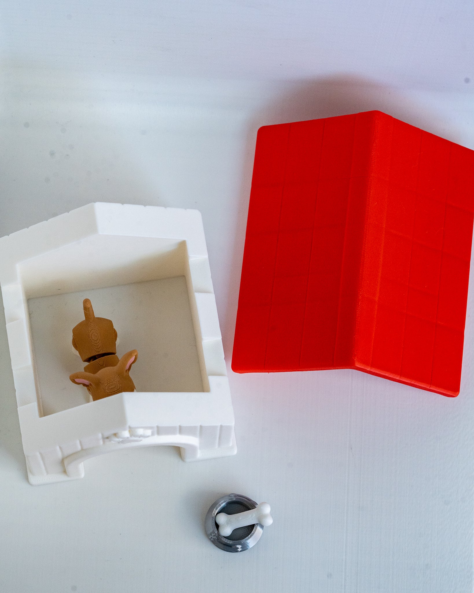 A small toy or figurine displayed inside a white house, with a bright red roof and a small silver-and-white bowl on a plain white background.