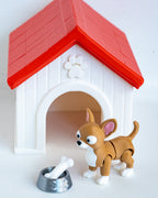 A small brown and white toy dog stands in front of a white dog house with a red roof, next to a silver bowl with a white bone, on a plain white background.