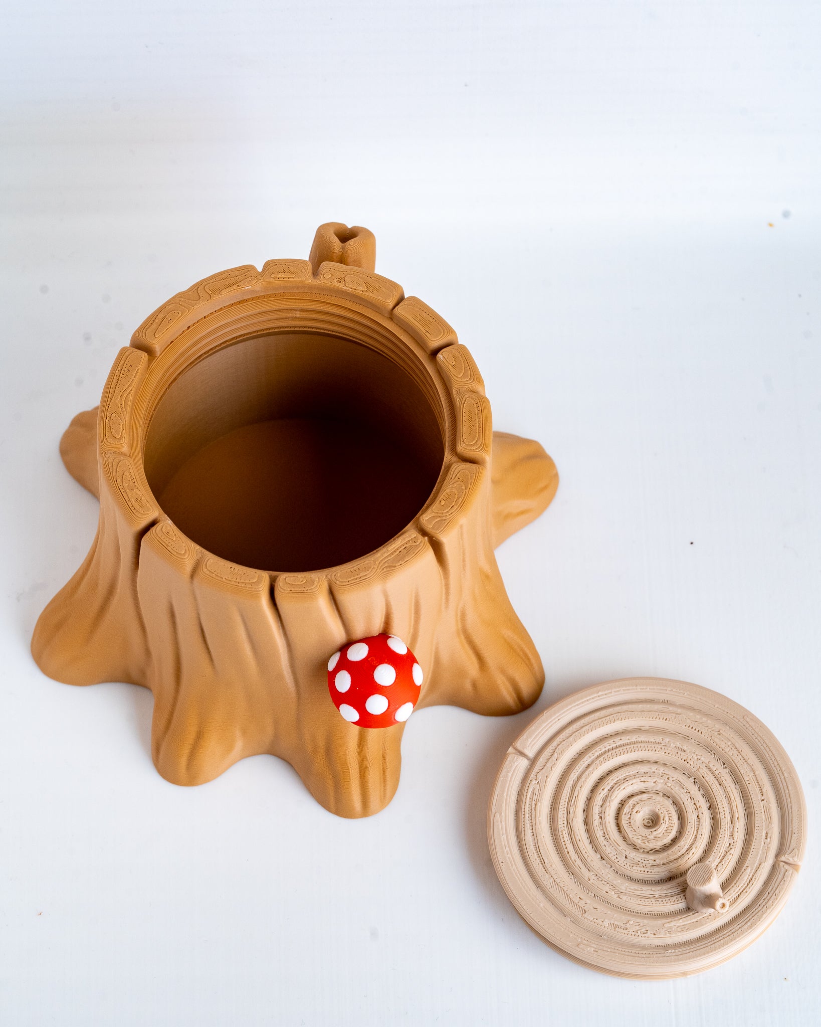 A tree stump-shaped plastic container with a small red and white polka dot mushroom accent, shown next to its circular beige lid on a white background.