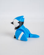 A small blue bird figurine with black and white markings, posed sitting on a plain light gray background.
