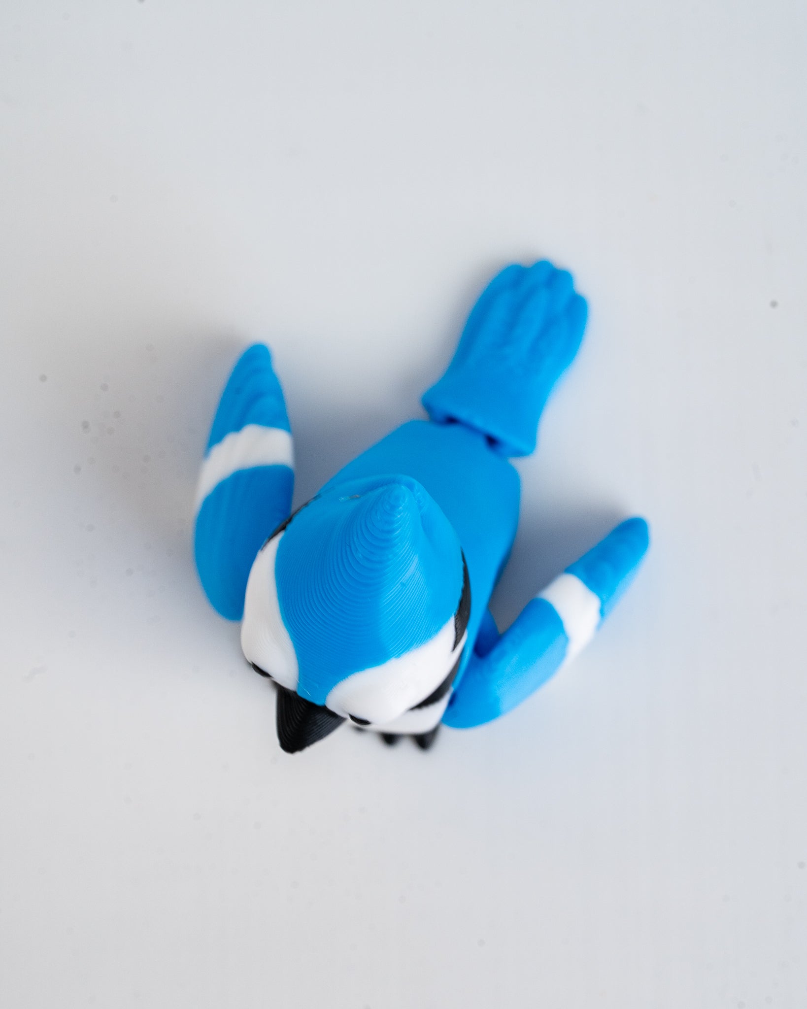 A small blue bird figurine or toy with white and black markings, photographed from above on a plain light background.