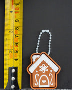 Mini gingerbread house clicker keychain next to measuring tape for scale
