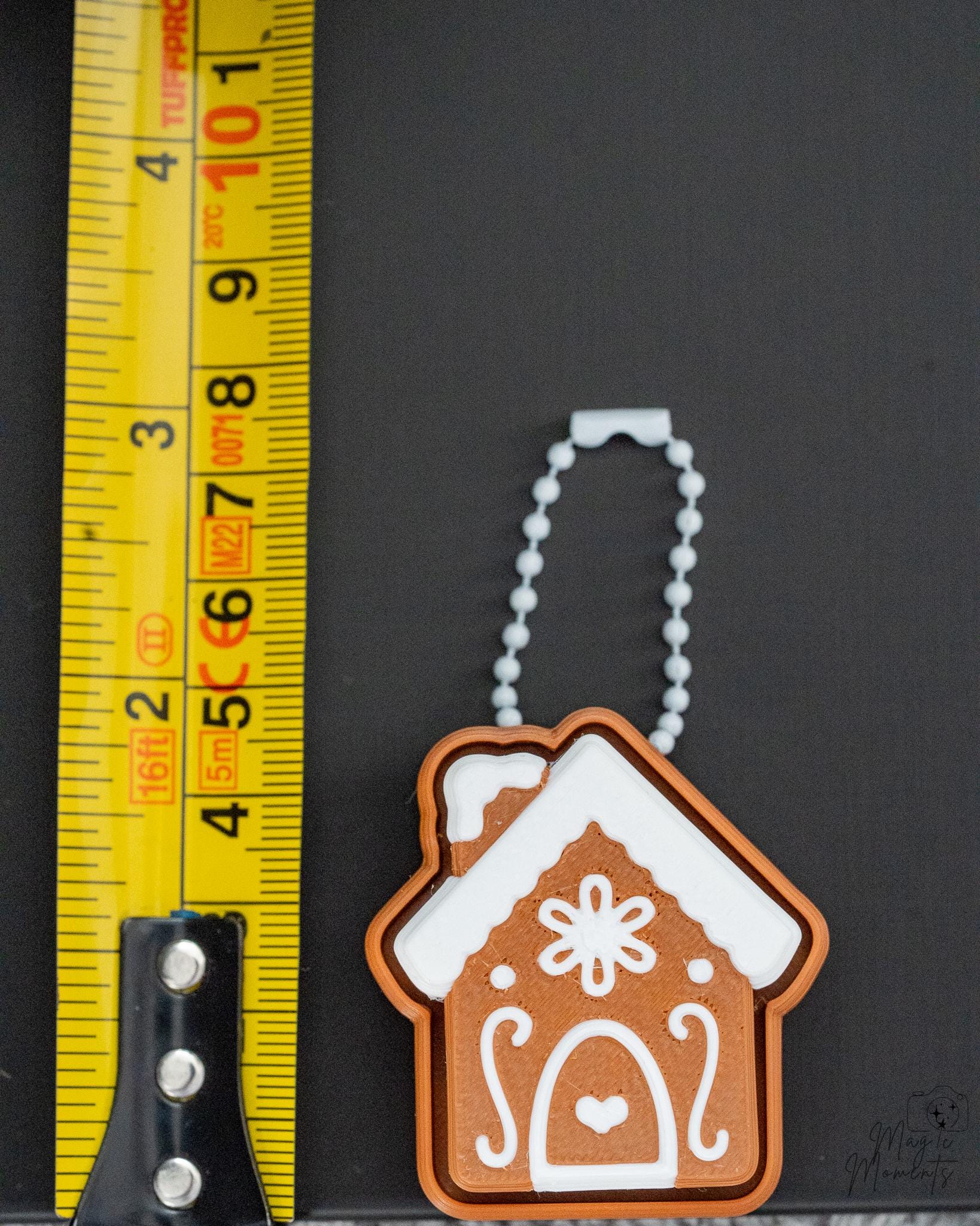 Mini gingerbread house clicker keychain next to measuring tape for scale