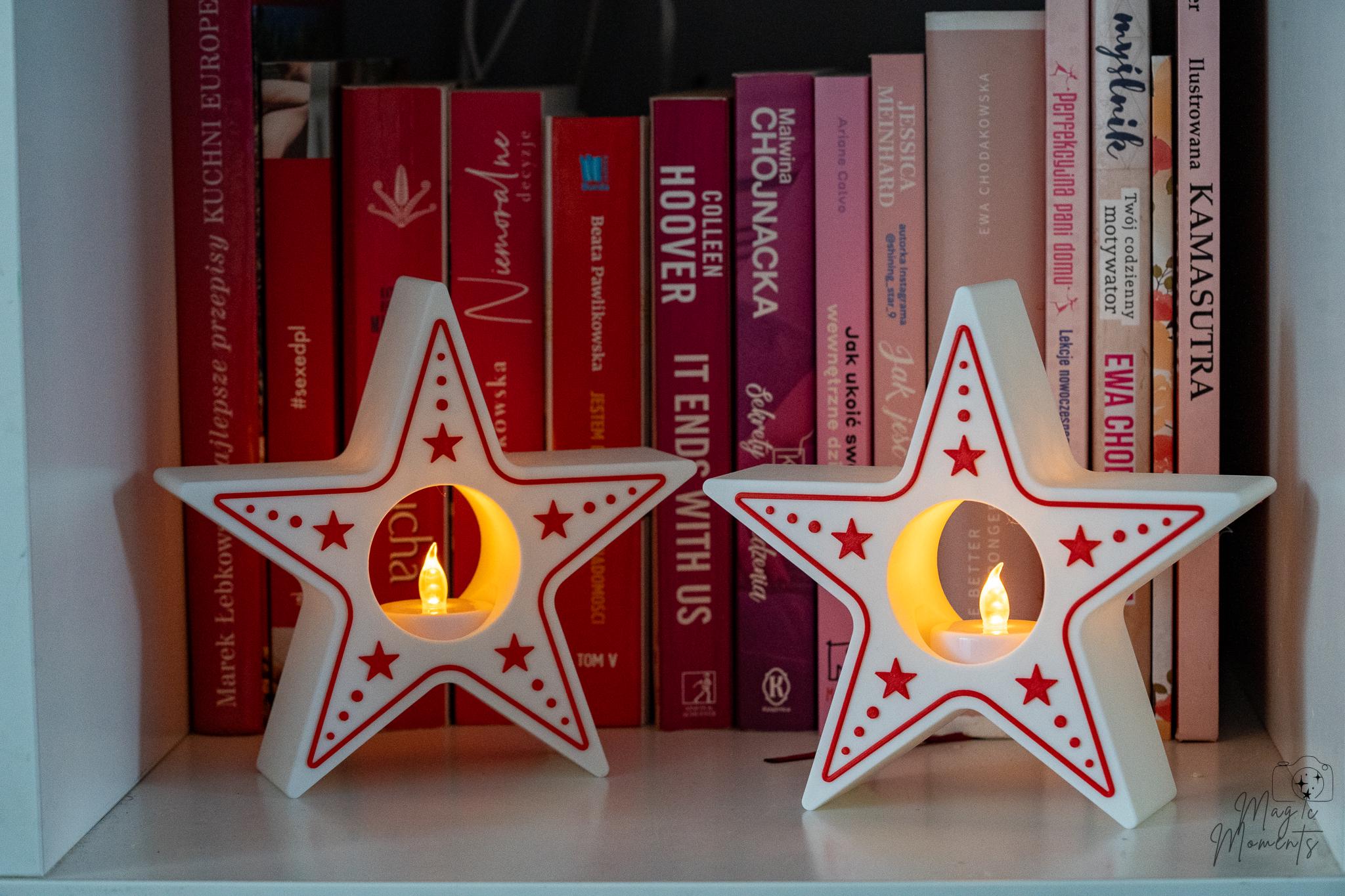Two star-shaped candle holders with candles on a shelf with books in the background.