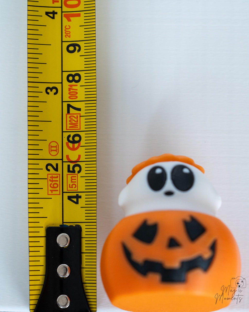 Ghost pumpkin figure with jack o lantern face next to measuring tape for scale
