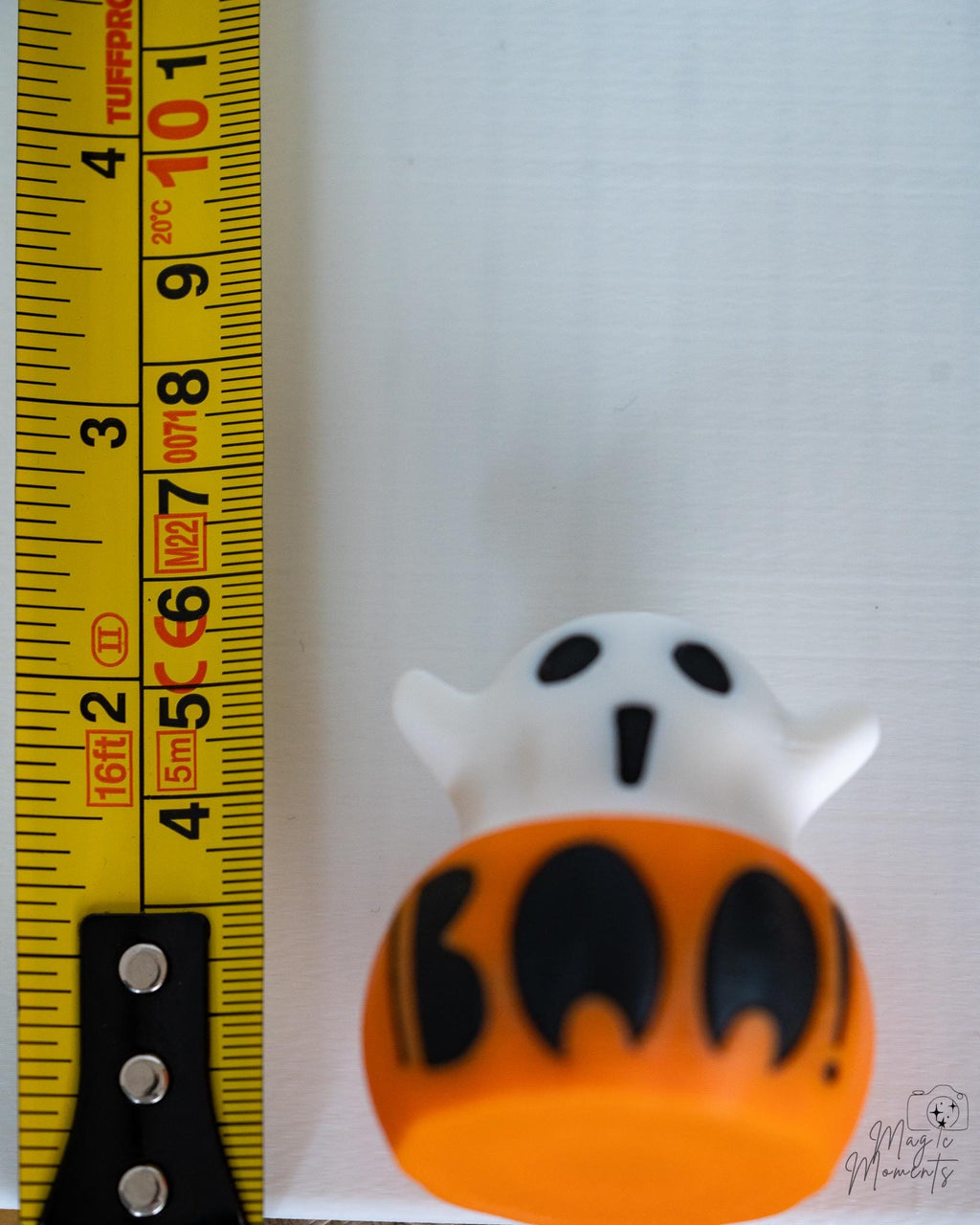 Ghost pumpkin clicker with black pumpkin cut out design next to measuring tape for scale