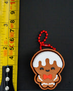 Gingerbread man keychain with a red bow tie next to a ruler on a black background