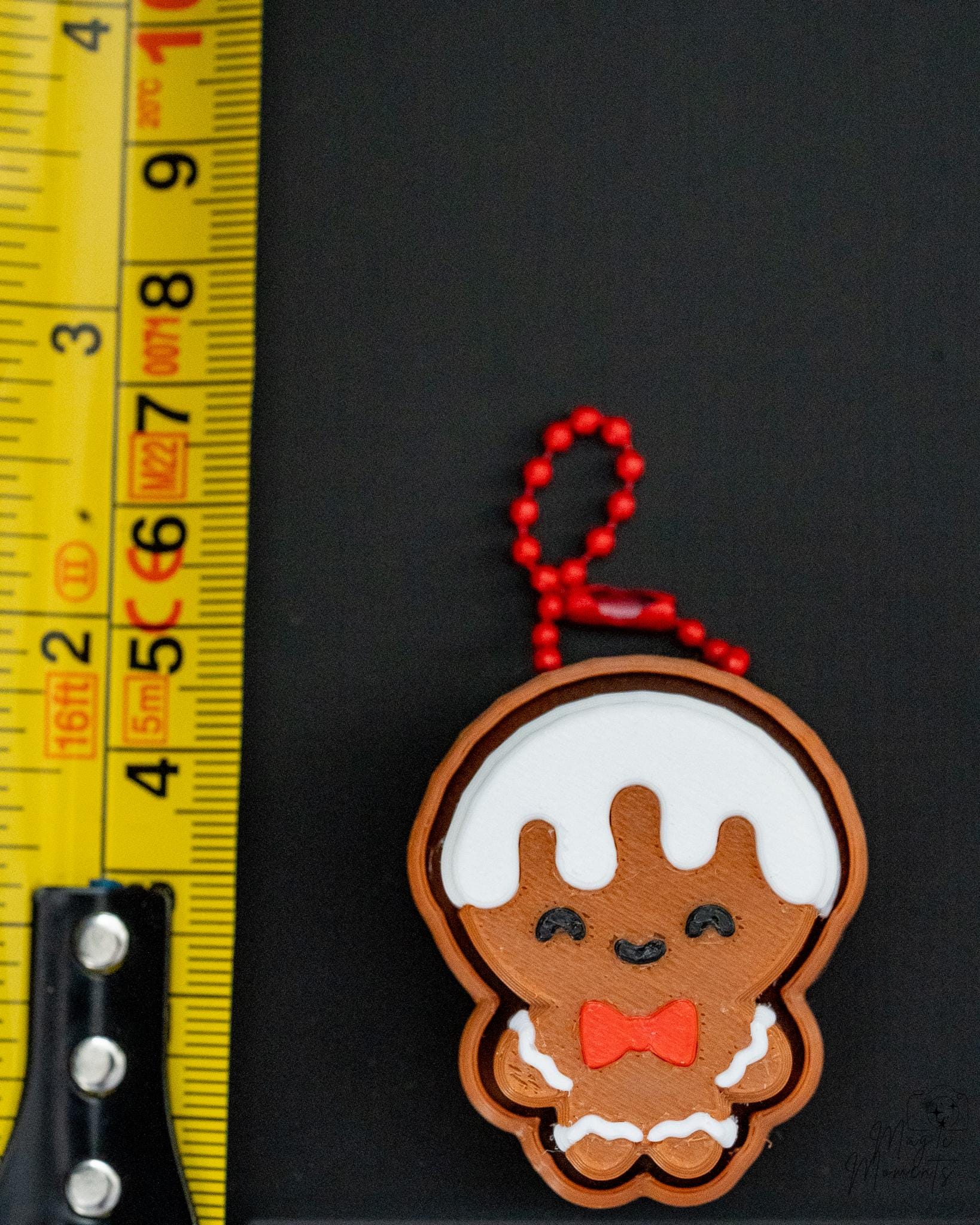 Gingerbread man keychain with a red bow tie next to a ruler on a black background