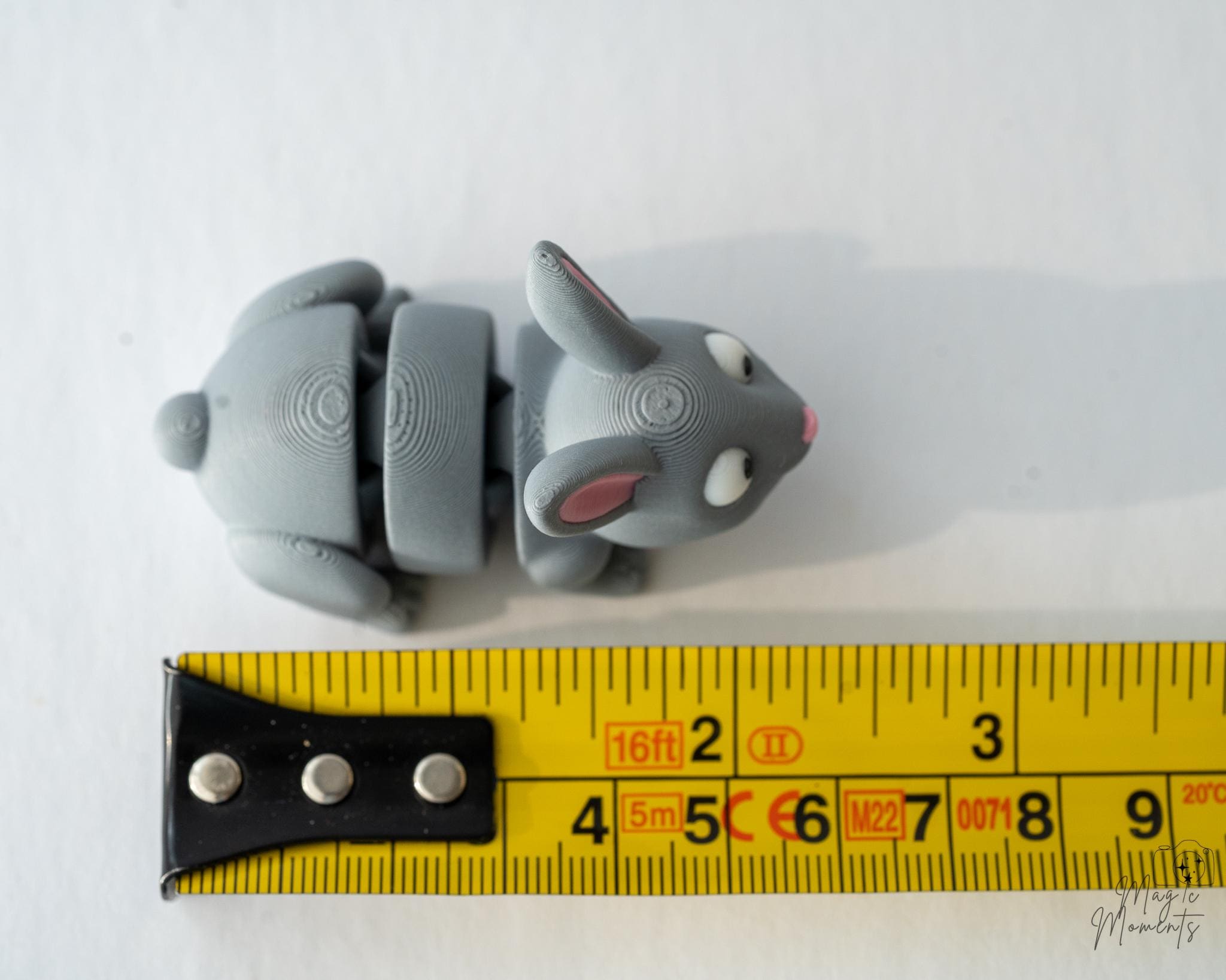 Gray rabbit figurine with measurement tape for scale on a white background