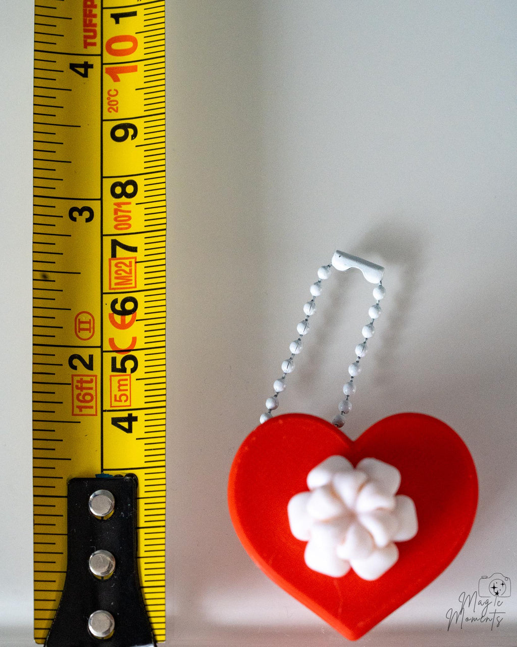 white heart clicker ornament next to measuring tape for scale
