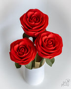 Three red roses in a white vase on a white background