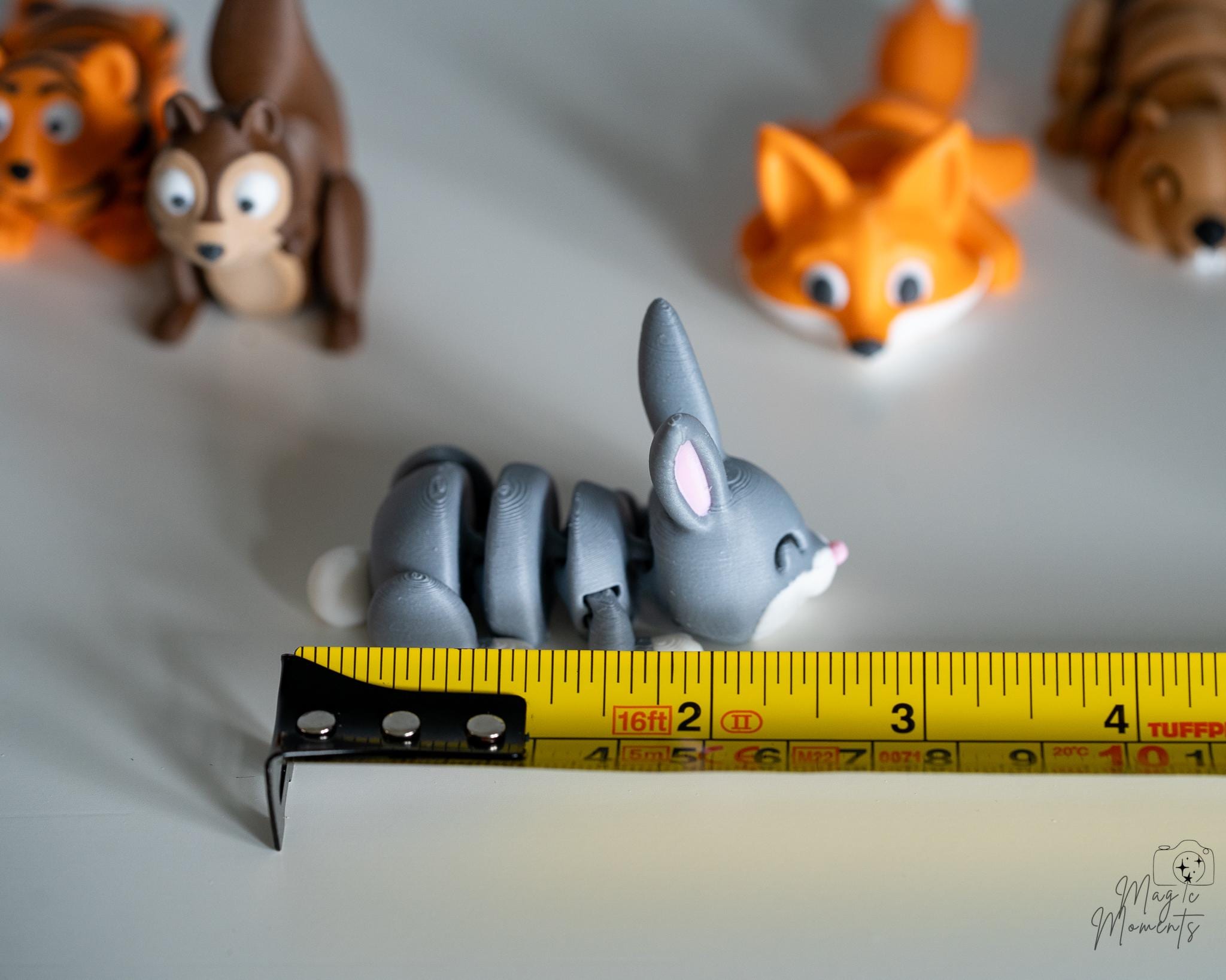 Small gray bunny figurine with a yellow measuring tape for scale on a light background