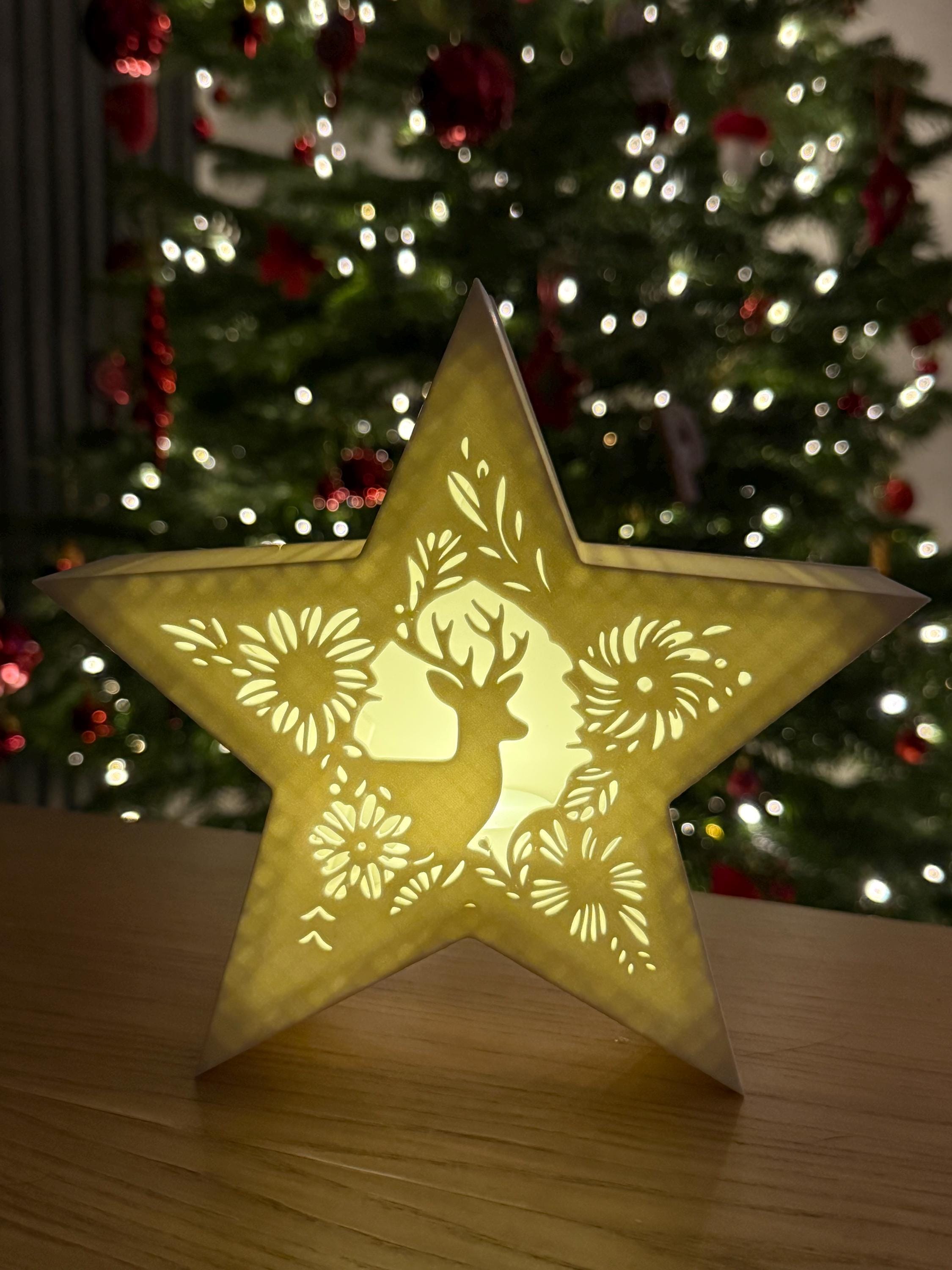 Decorative star-shaped tealight holder with reindeer design in front of a Christmas tree.