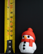 Mini knitted snowman figurine with red hat and scarf next to measuring tape for a scale