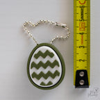 Mini Easter egg clicker with hanging chain next to measuring tape for scale