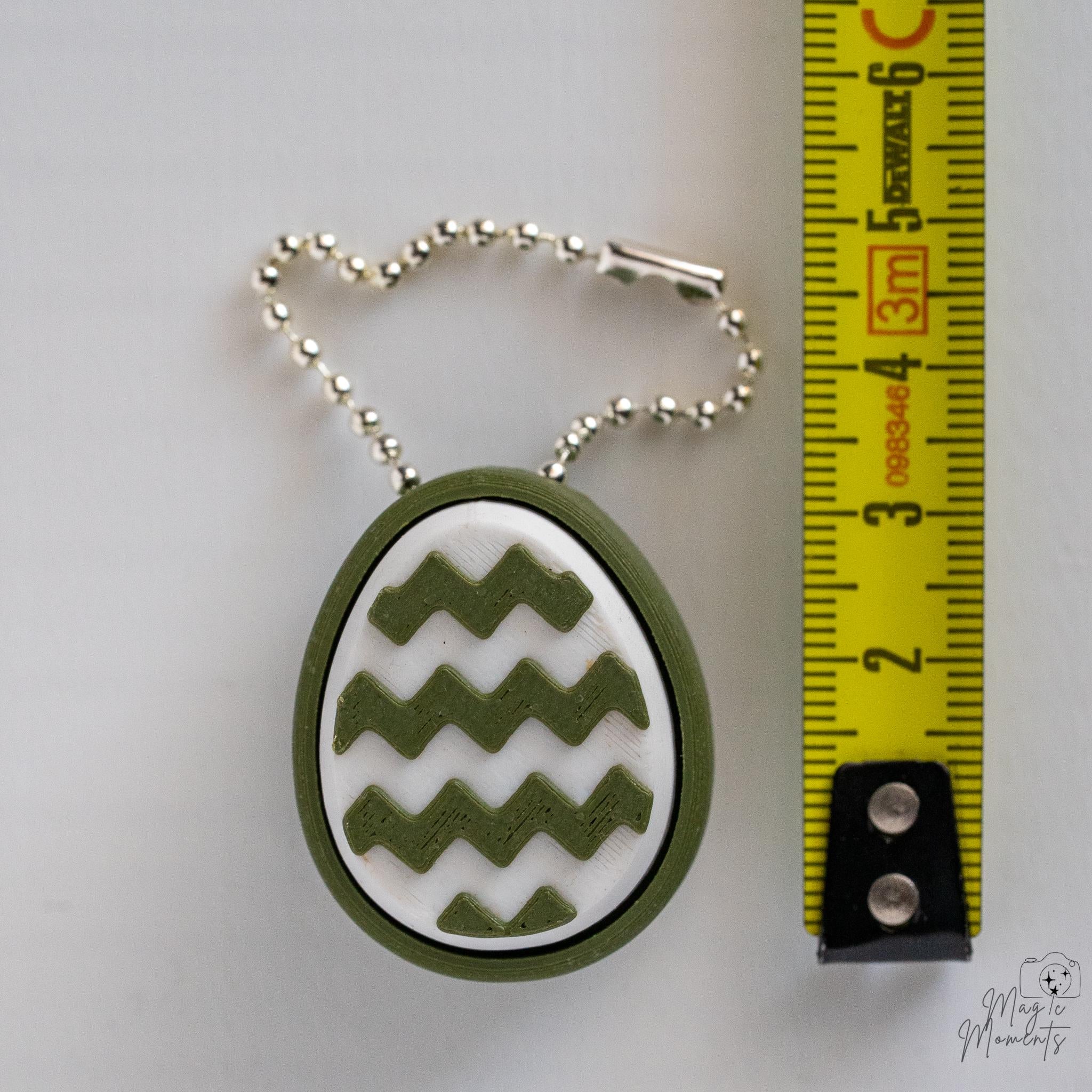 Mini Easter egg clicker with hanging chain next to measuring tape for scale