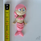 pink mermaid figurine next to measuring tape for scale