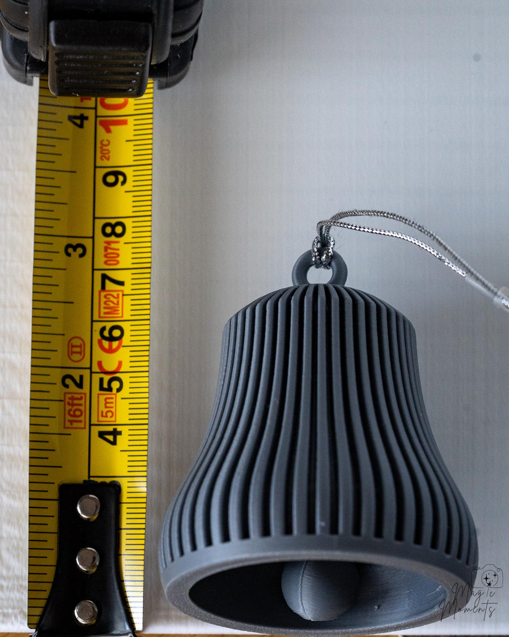 grey ribbed christmas bell ornament next to measuring tape for scale