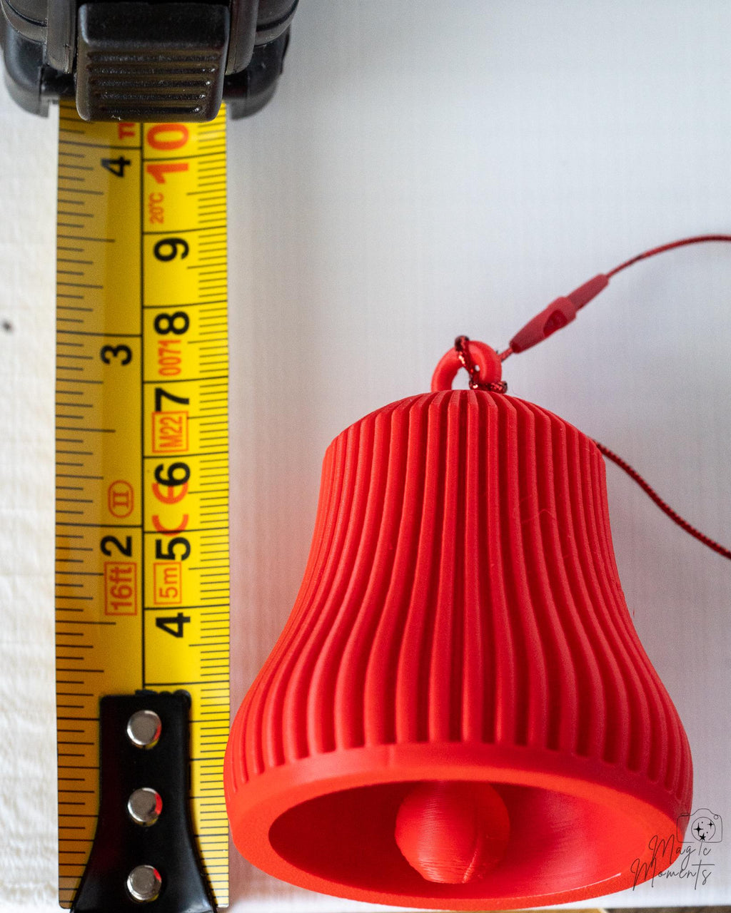 red ribbed christmas bell ornament next to measuring tape for scale