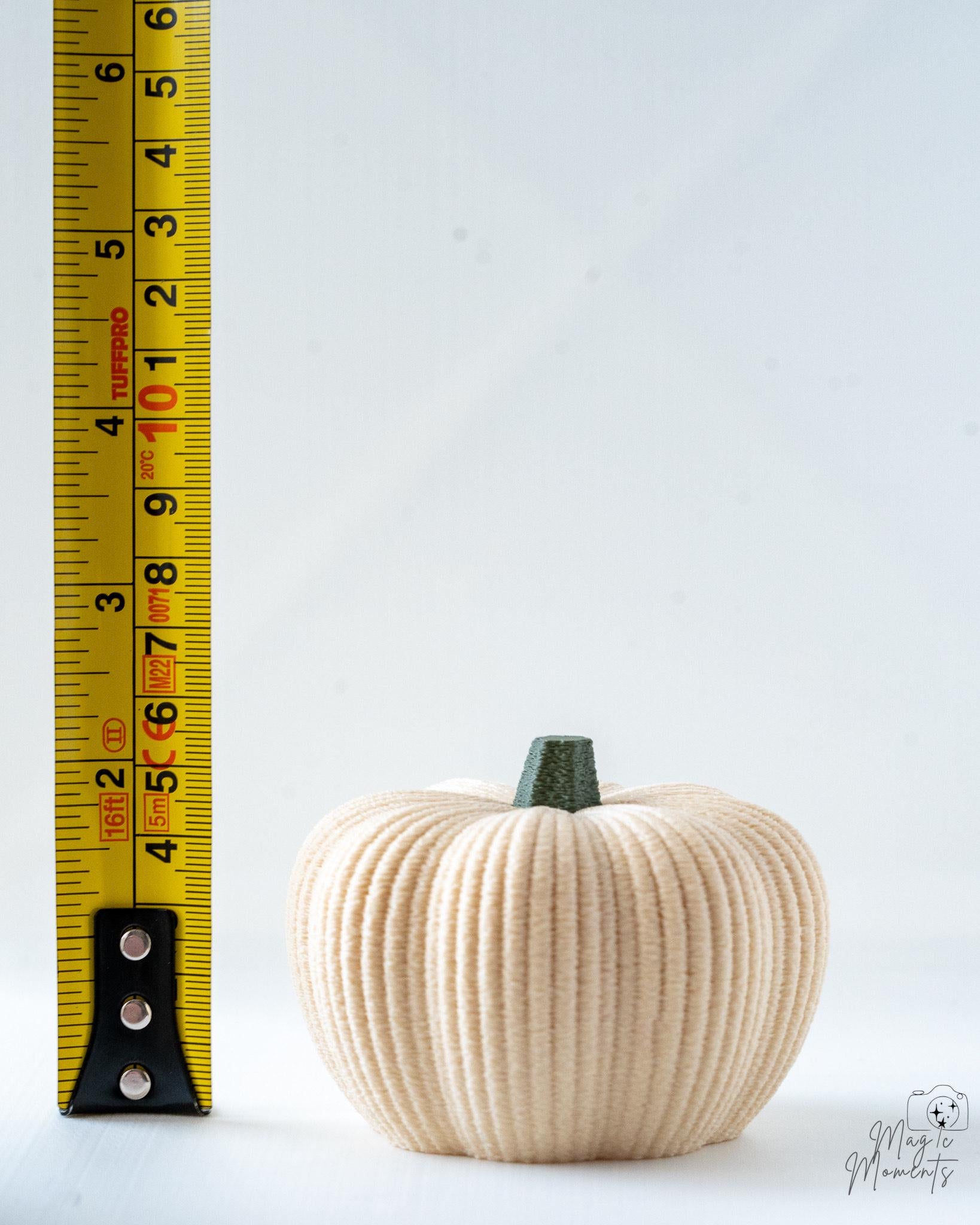 beige fuzzy pumpkin next to measuring tape for scale