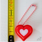 Layered heart clicker with pink hanging loop next to measuring tape for scale