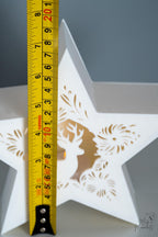 White star-shaped decorative item with cut-out patterns, measured by a yellow ruler 
